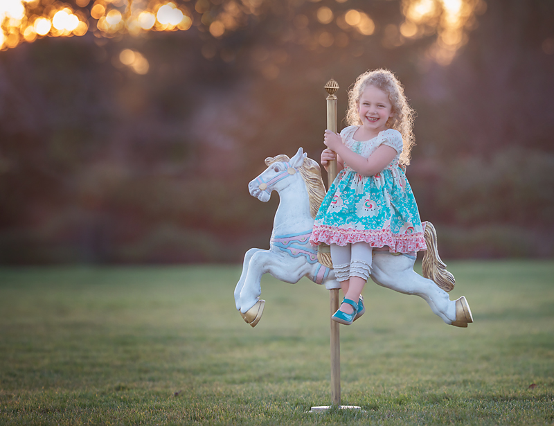 curly haired girl riding carousel horse in grass