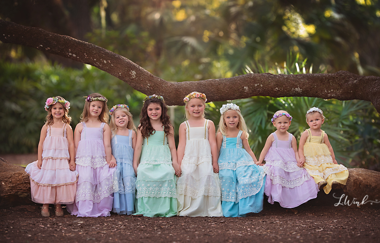 group of little girls in many different colors of princess dresses sitting on a log