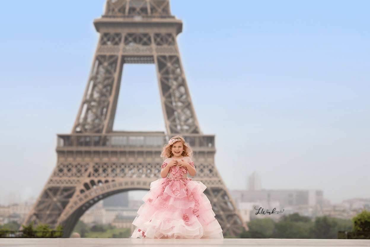 Laughing girl in fancy pink dress in front of Eiffel Tower