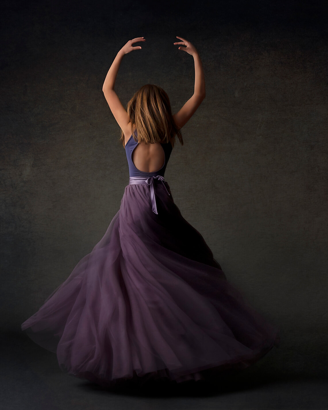 Studio portrait of the back of a L.A. dancer with arms up in purple skirt